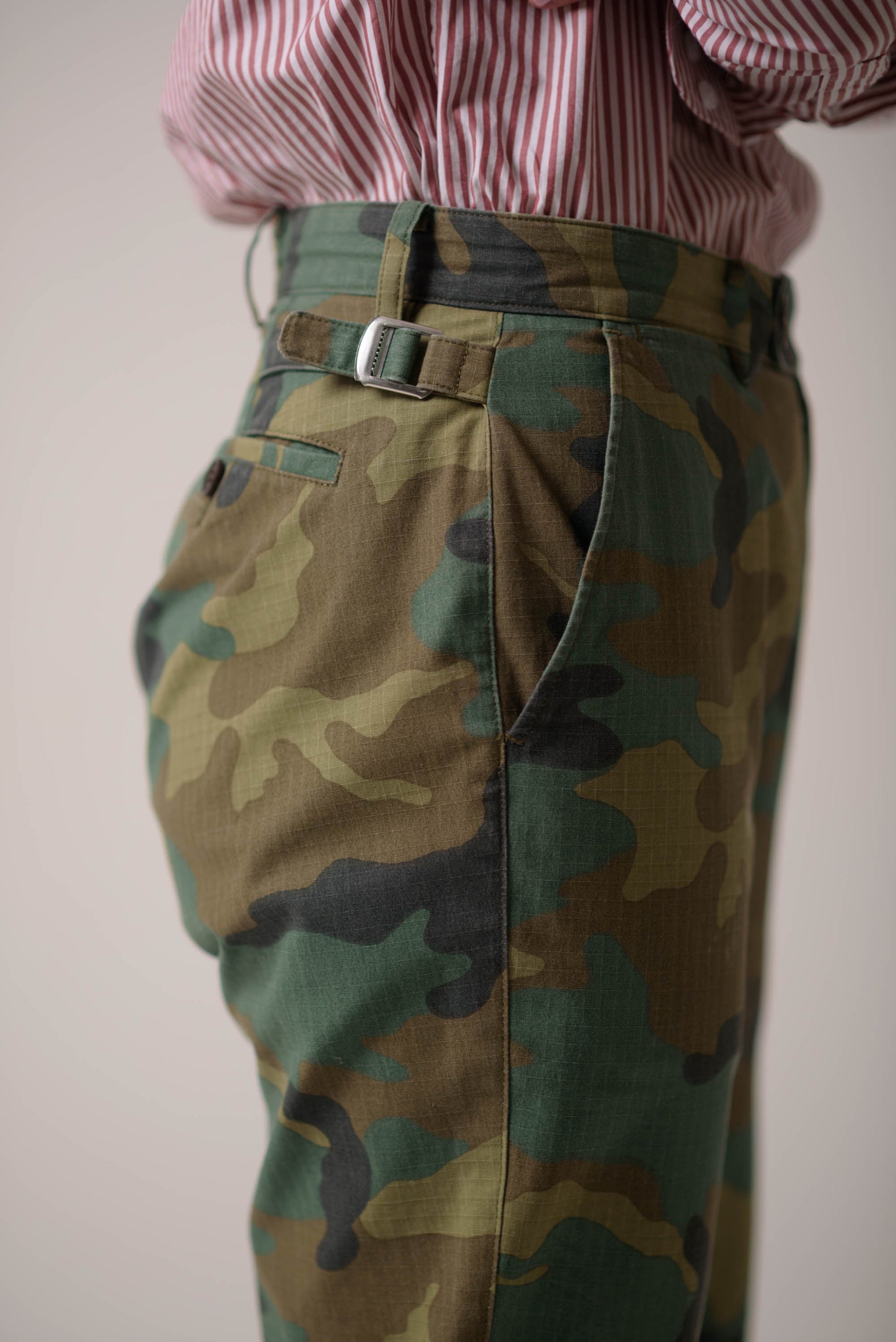 Camouflage pants with a belt and a red and white striped shirt on a plain background
