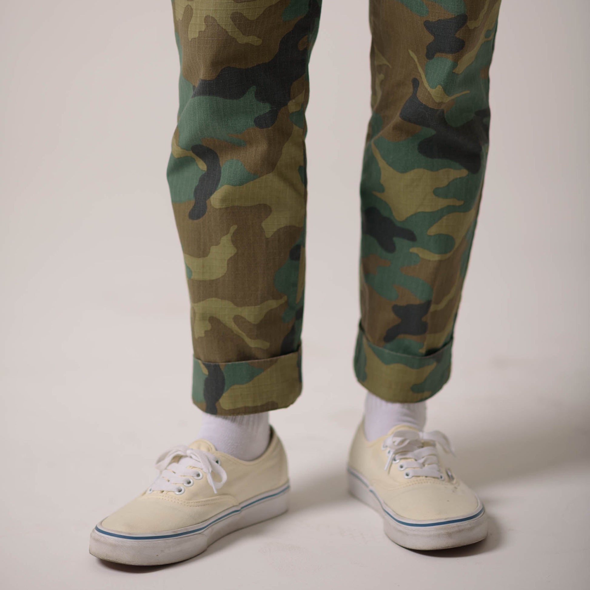 Camouflage pants worn with white sneakers on a plain background
