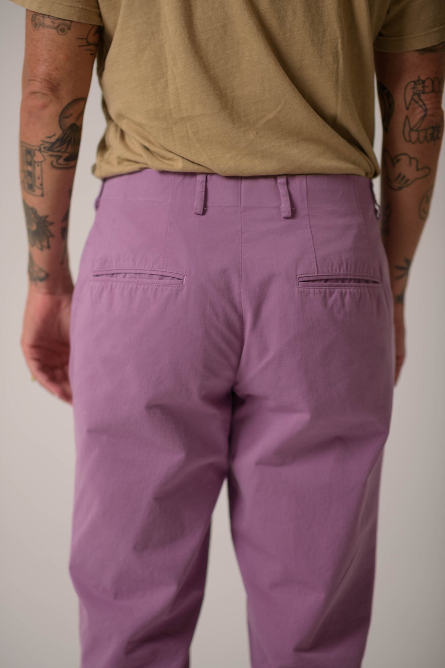 Person wearing purple pants and a beige shirt against a plain background