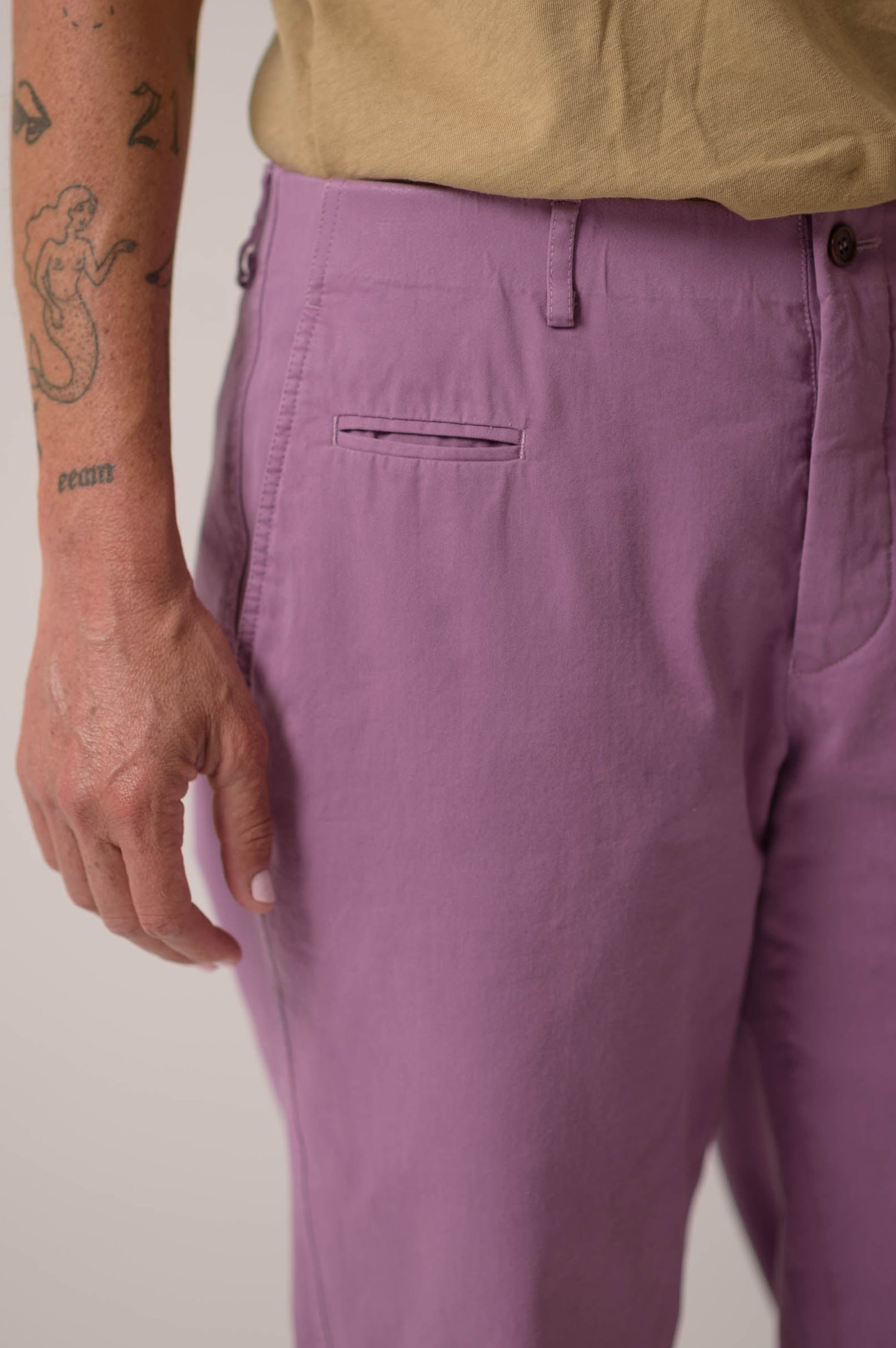 Person wearing purple pants and a beige shirt with a plain background
